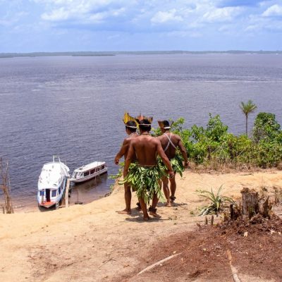 Dois homens indígenas observam barcos no rio Amazonas.