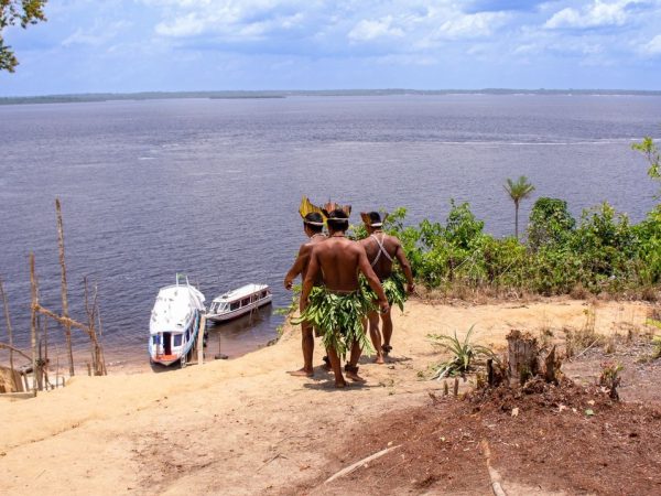 Dois homens indígenas observam barcos no rio Amazonas.
