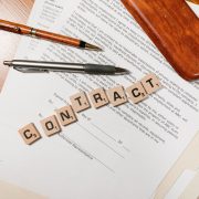 Documentos contratuais sobre uma mesa, com peças formando a palavra “CONTRACT” e uma caneta ao lado
