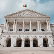 Vista frontal do Palácio de São Bento, sede do Parlamento português, com a bandeira nacional hasteada.