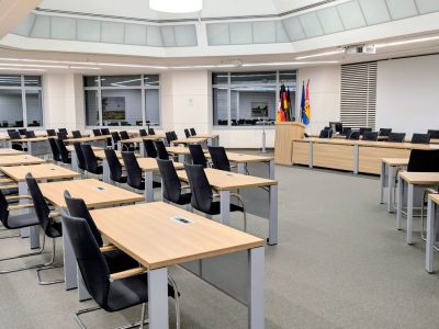 Sala ampla e moderna de reunião institucional, com mesas organizadas e bandeiras ao fundo.