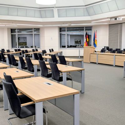 Sala ampla e moderna de reunião institucional, com mesas organizadas e bandeiras ao fundo.