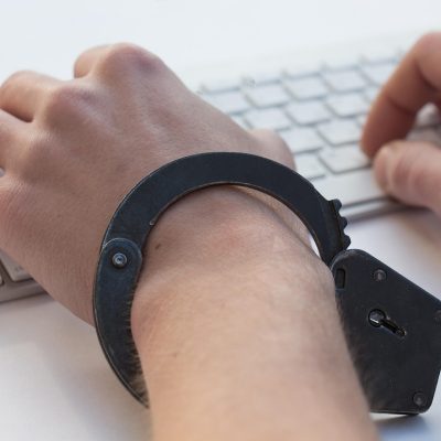 Mãos algemadas sobre um teclado, em uma representação conceitual da dependência em jogos de azar e da perda de controle.