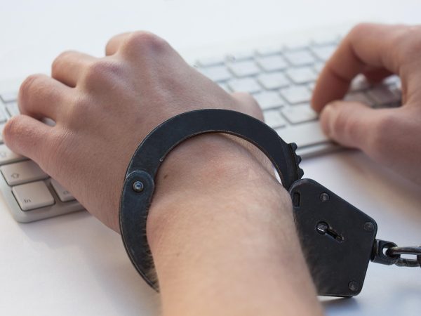 Mãos algemadas sobre um teclado, em uma representação conceitual da dependência em jogos de azar e da perda de controle.