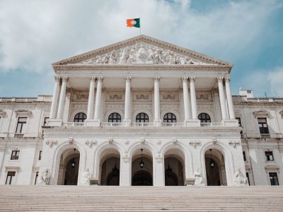 Vista frontal do Palácio de São Bento, sede do Parlamento português, com a bandeira nacional hasteada.