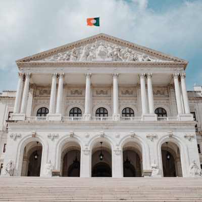 Vista frontal do Palácio de São Bento, sede do Parlamento português, com a bandeira nacional hasteada.